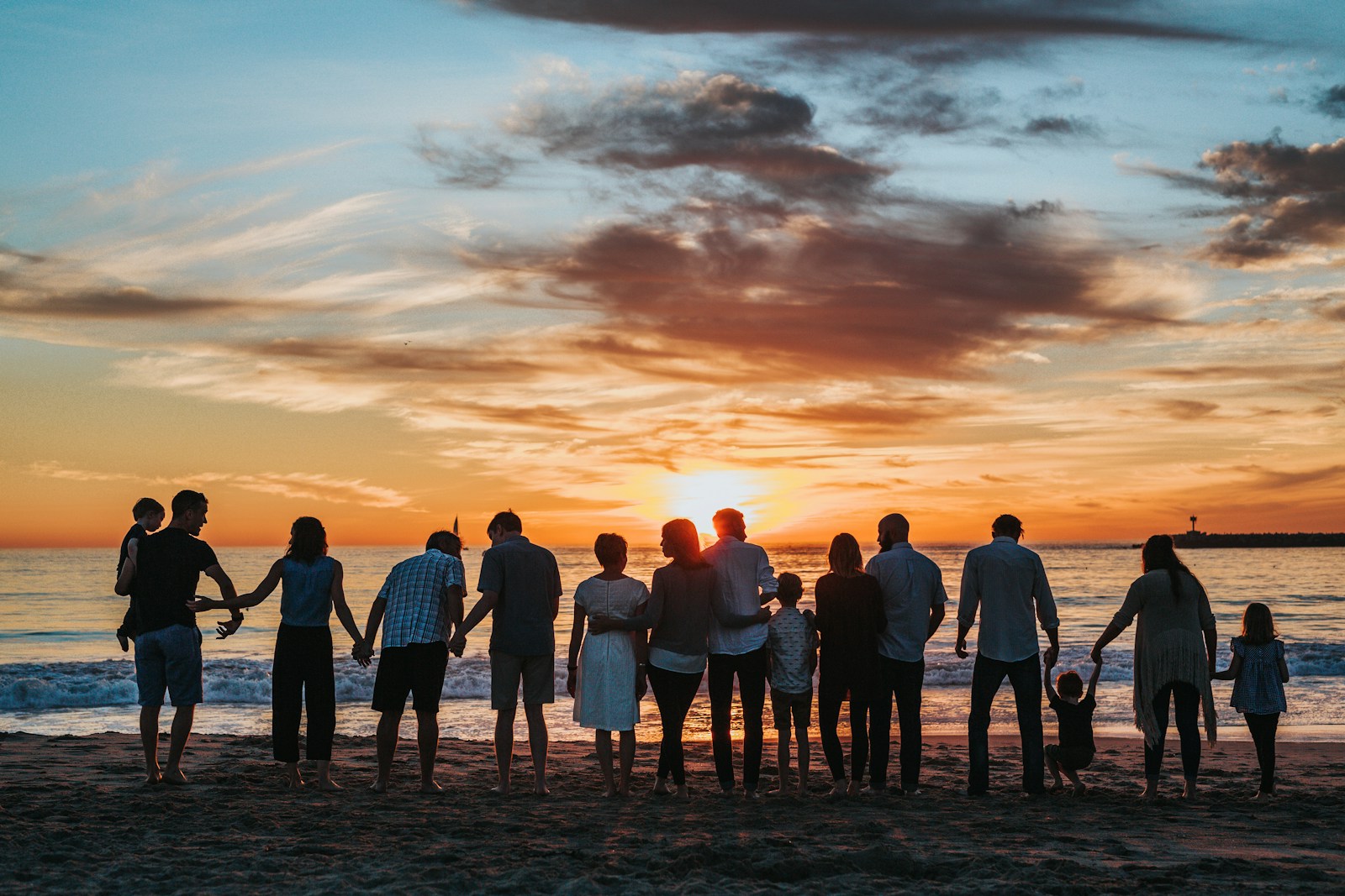 Erwachsene und Kinder am Meer bei Sonnenuntergang, überwiegend von hinten – Symbolfoto